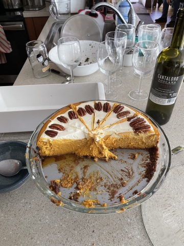 half a cheesecake on a cake stand. dirty dishes in the background.